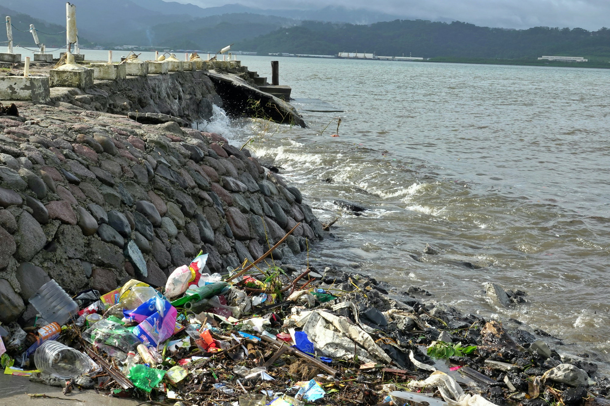 trash-litters-the-shoreline-next-to-a-stone-wall-.jpg Trash litters the shoreline next to a stone wall.